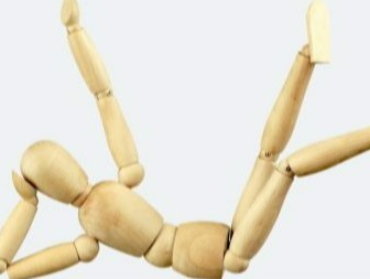 Manichino di legno seduto a terra con sfondo bianco usato per studio delle forme del corpo umano