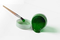 Vasetto con colore verde che fuoriesce e pennello intinto nel colore
